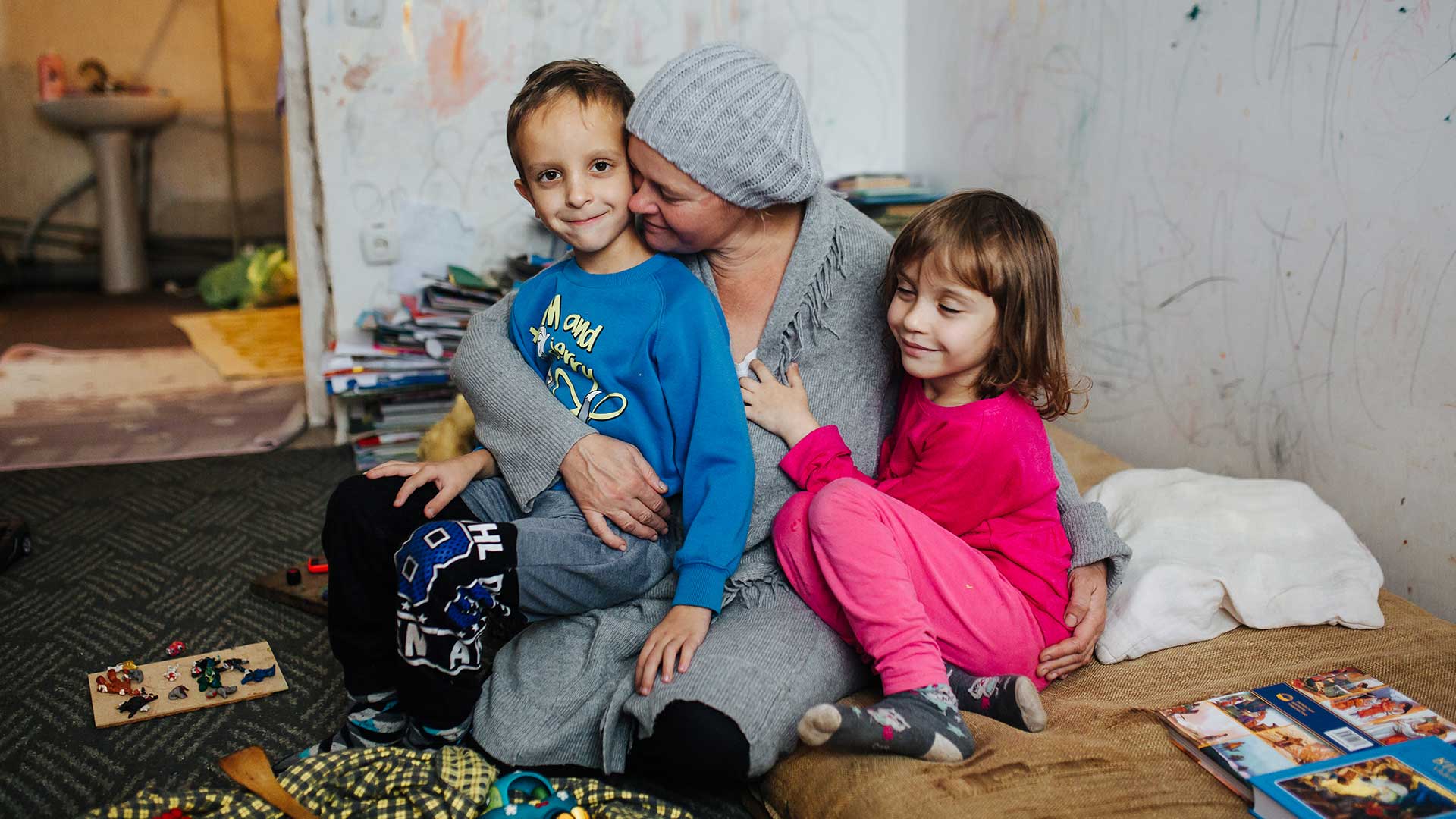 A family sit on a mattress on the floor.